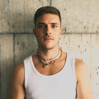 Man wearing a long necklace with gold and silver chains adorned with vintage rings